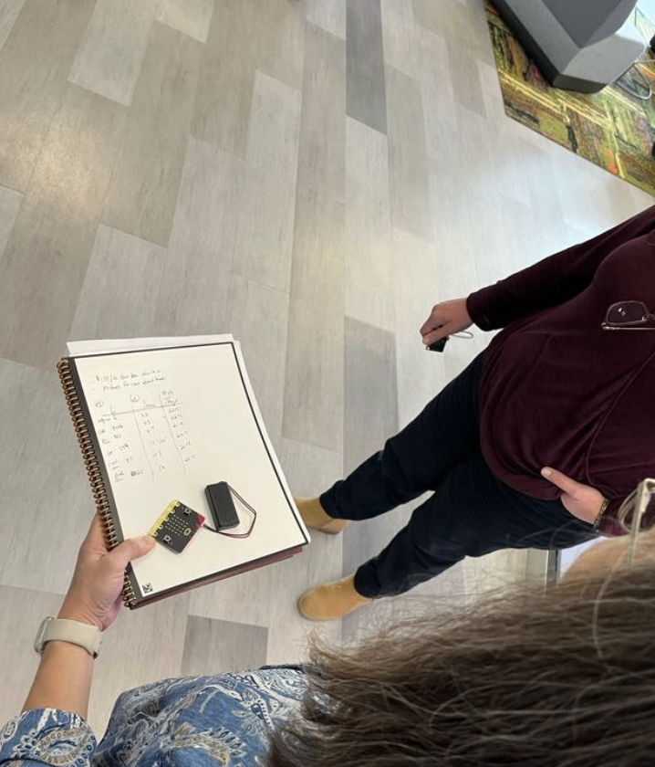 An educator holds a Micro:bit and a notebook with data. 